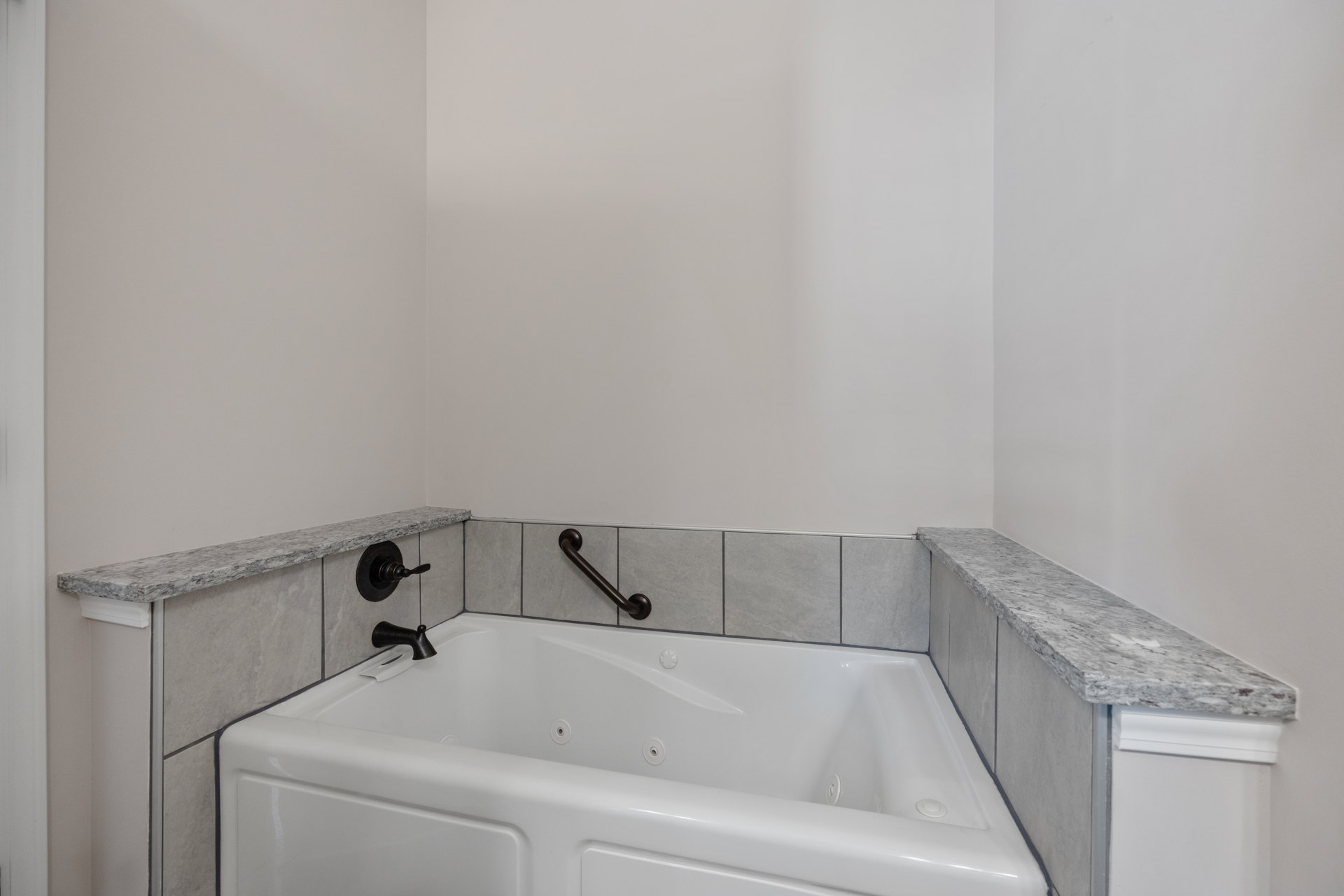 White bathtub with chrome faucet and overhead metal grab bar, set against a tiled bathroom wall