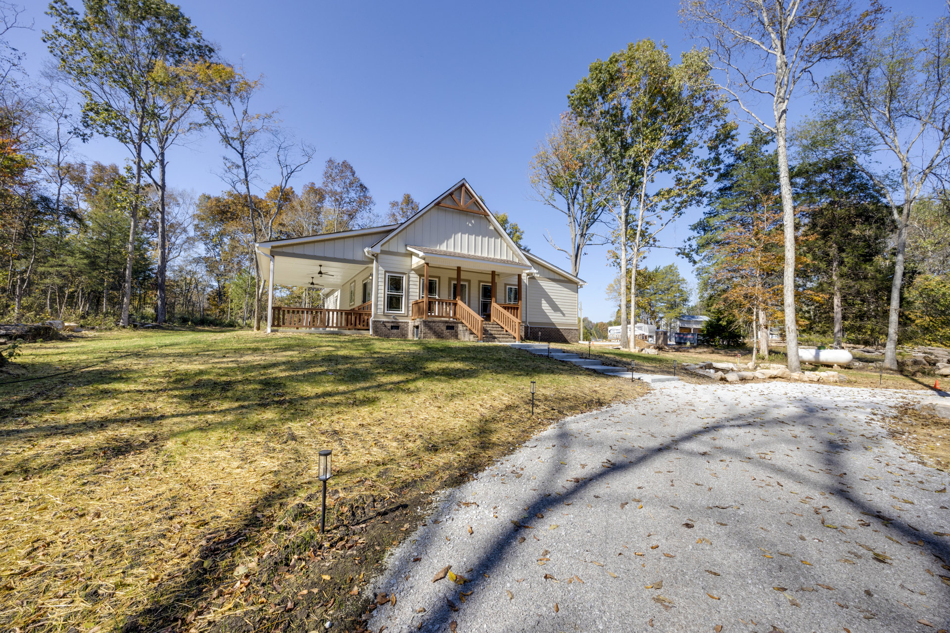 Two-story house with white siding, covered front porch, concrete walkway, green lawn, mature trees in background, and tree shadows on driveway