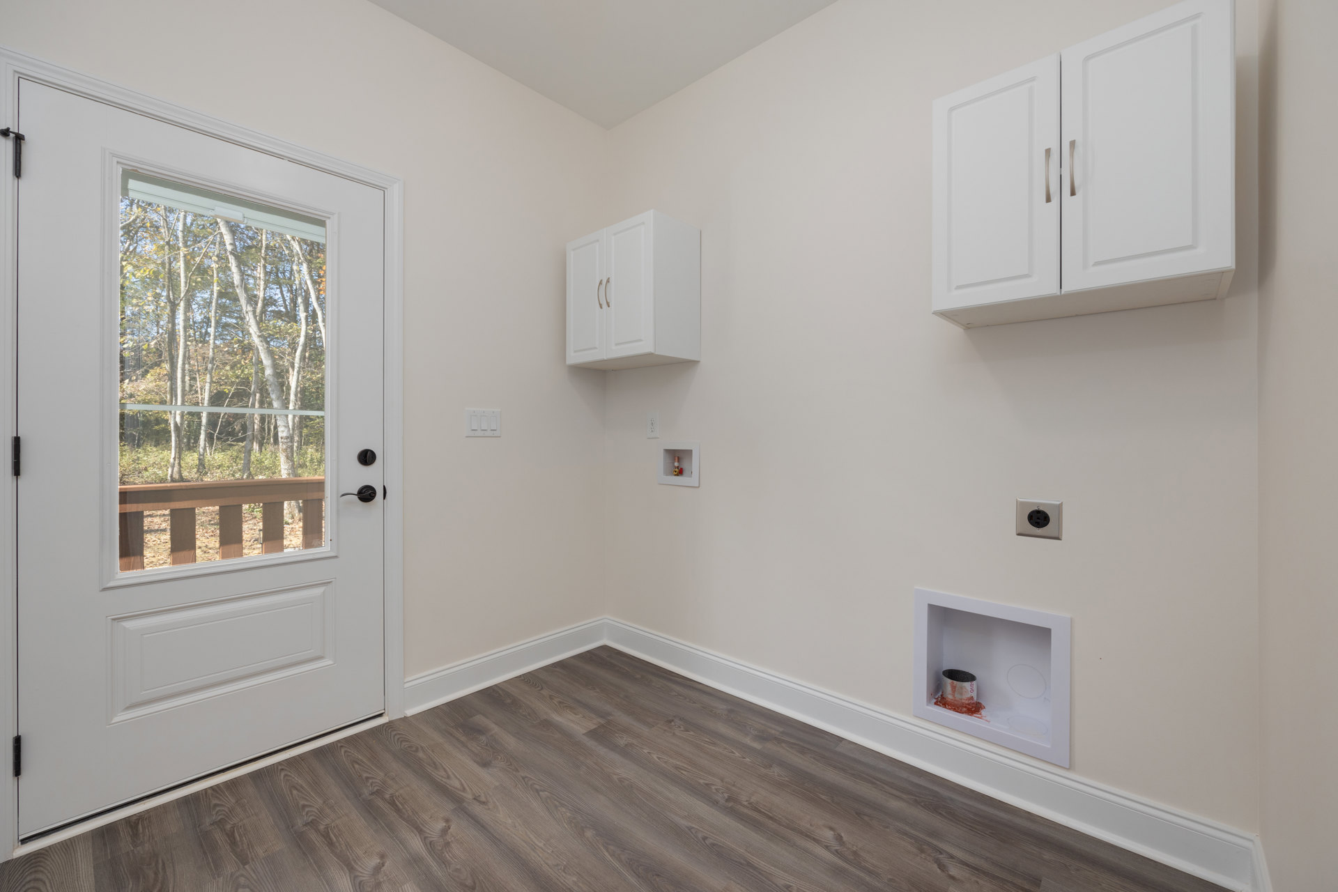White walls, wood flooring with white baseboards, white cabinet with metal handles, power outlet, wooden railing visible through window, two doors