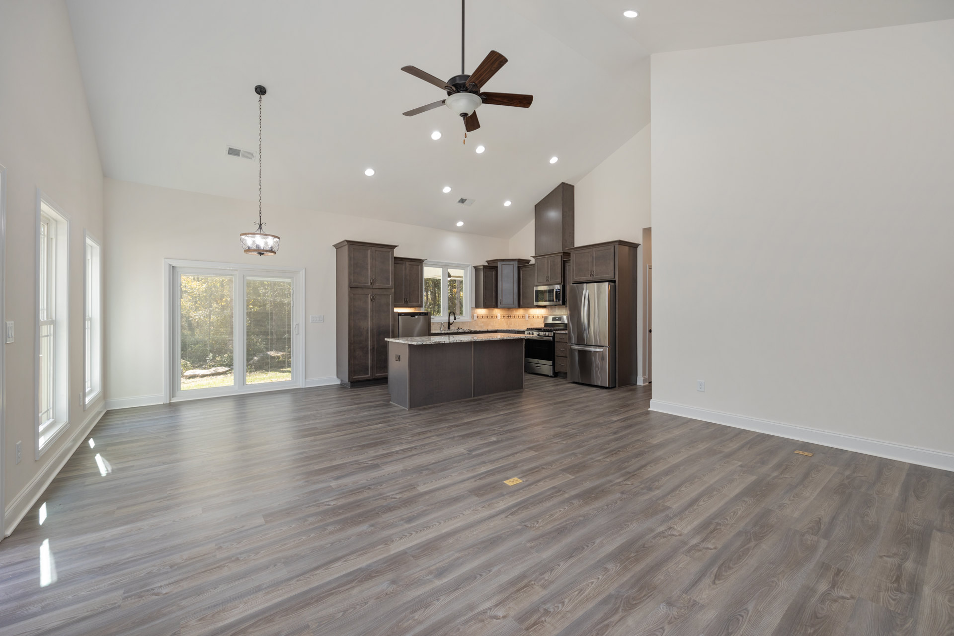 Spacious kitchen and dining area with wood flooring, stainless steel refrigerator, ceiling fan with light fixture, chain hanging from ceiling, window with blinds, and yellow mark