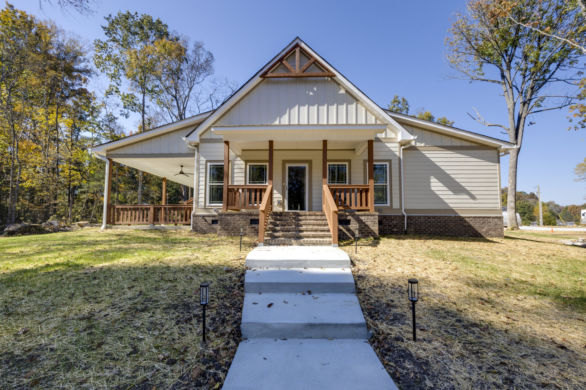 Two-story brick house with covered front porch, white columns, concrete steps, wooden railing, and mature tree in landscaped yard