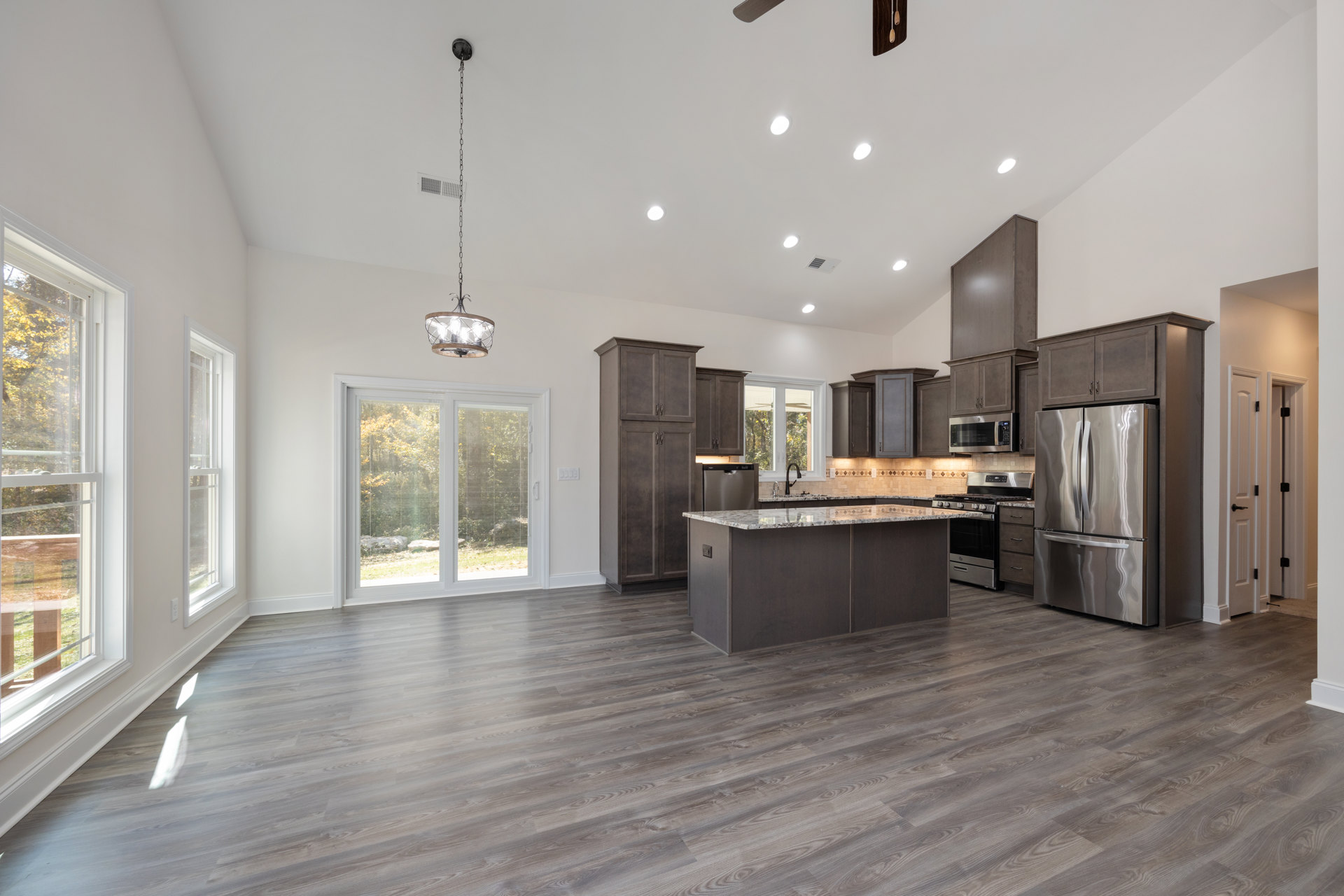 Spacious kitchen featuring a large central island with white countertop, stainless steel double-door refrigerator, wood flooring, white cabinetry, ceiling vent, window with blinds