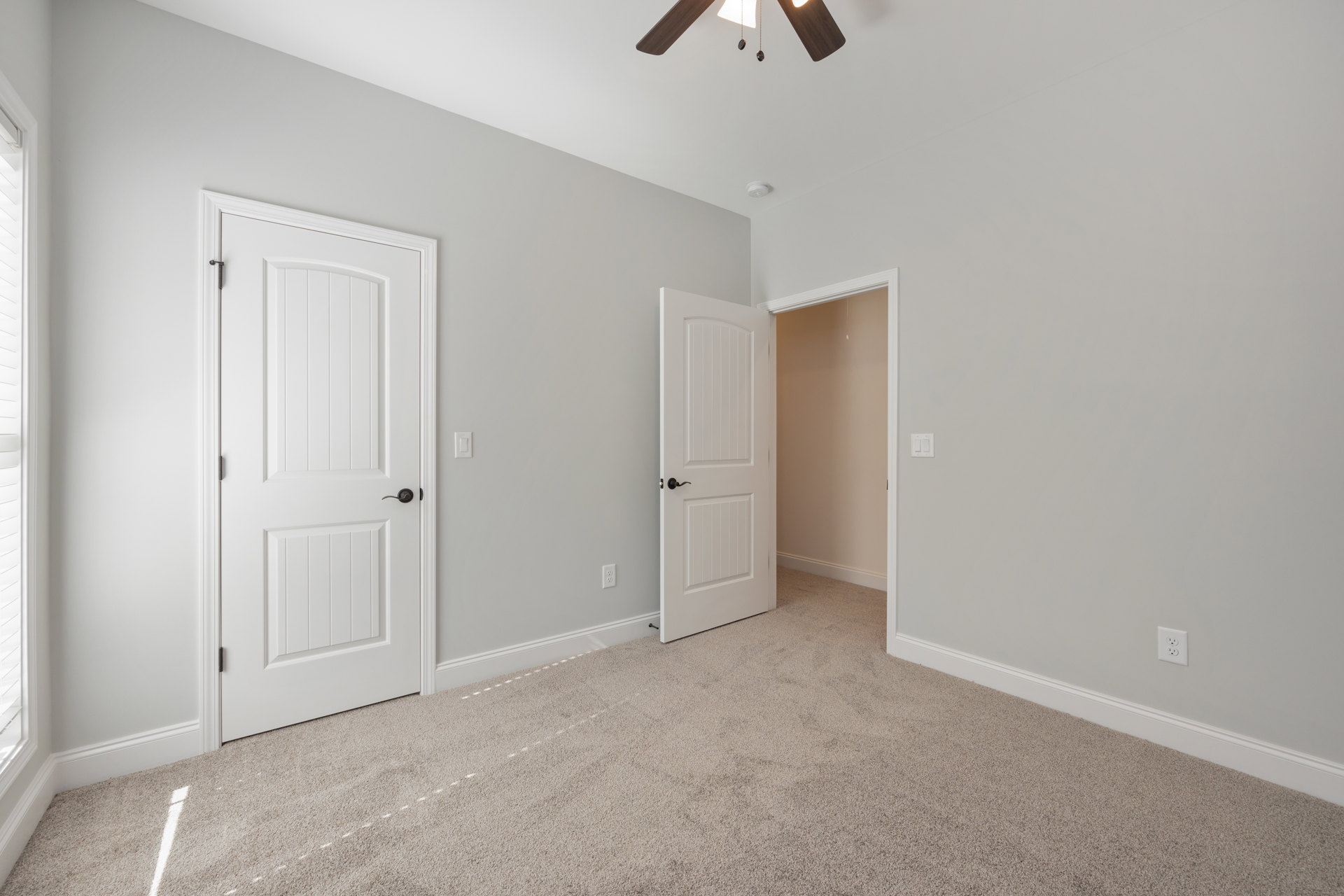 Bedroom with white plaster walls, ceiling fan, white doors with black handles, light fixture hanging by a chain, white trim and molding, hardwood flooring