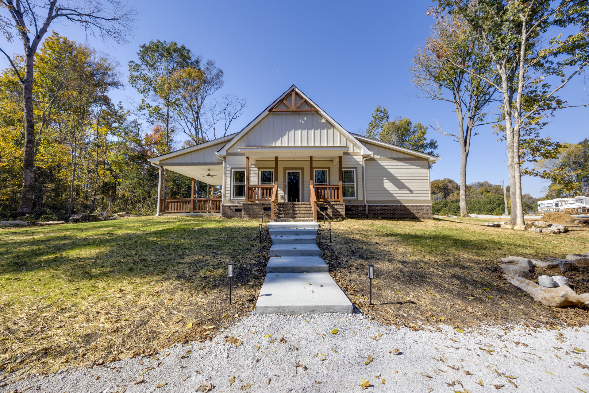 Two-story house with covered porch, concrete steps, and walkway bordered by grass and mature trees; white planters sit on rocks near the entrance.