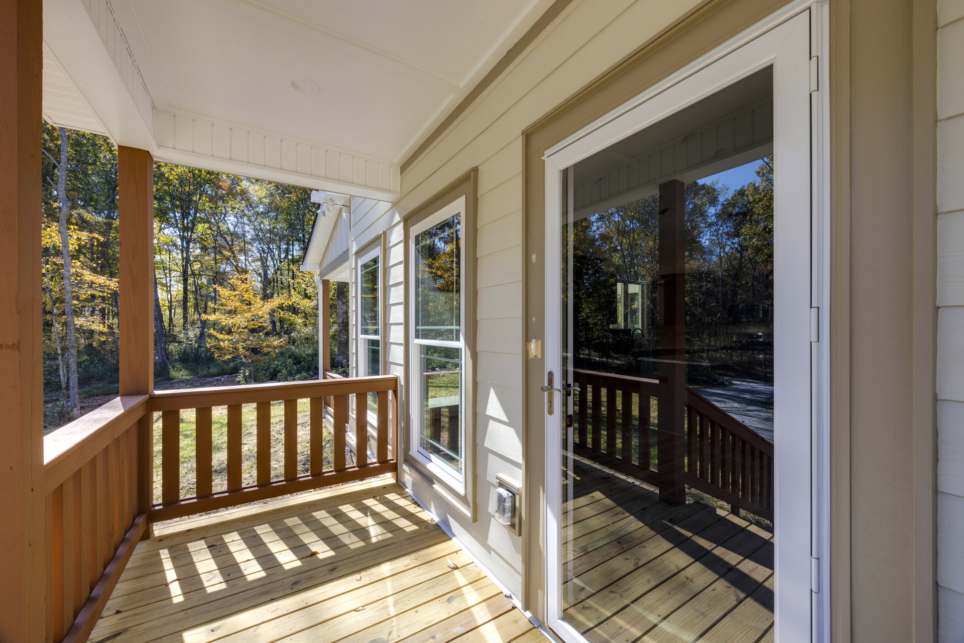 Porch with glass double doors, wooden railing, and deck overlooking trees and grassy yard