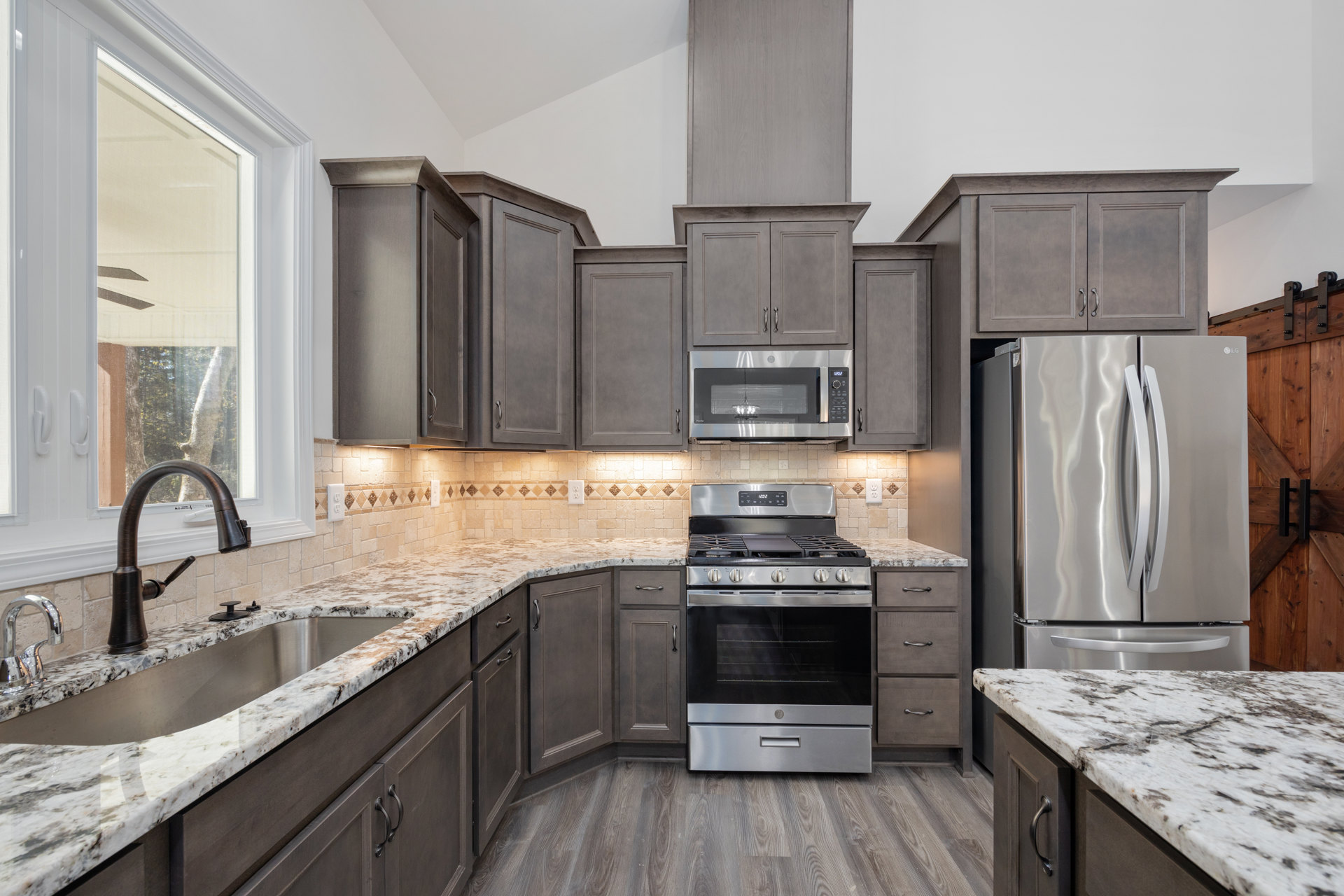Granite countertops, stainless steel stove and refrigerator, silver microwave with built-in light, white cabinetry, window with fan, modern sink fixtures