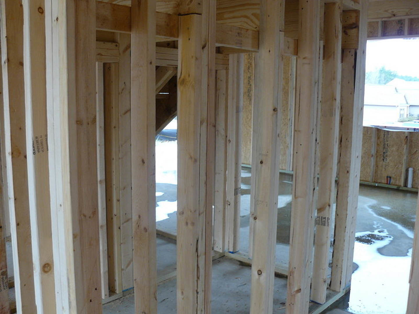 Exposed wood framing with vertical and horizontal beams, unfinished interior, visible insulation between studs