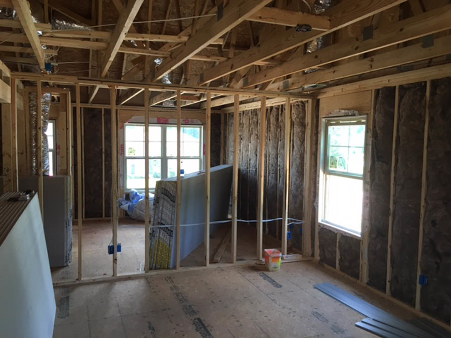 Sunlit room with white walls, large window framed in wood, exposed ceiling beams, and light hardwood flooring