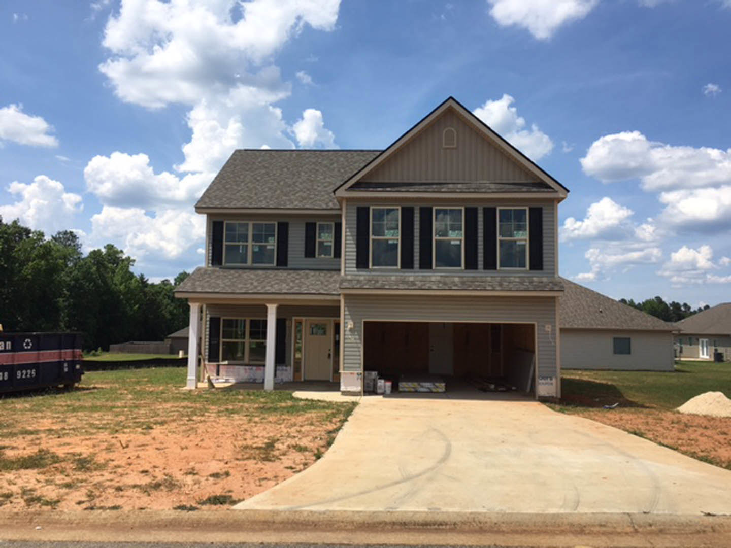 Two-story custom home with attached garage, gray siding, white trim, shingle roof, large windows, concrete driveway, and landscaped front yard with trees.