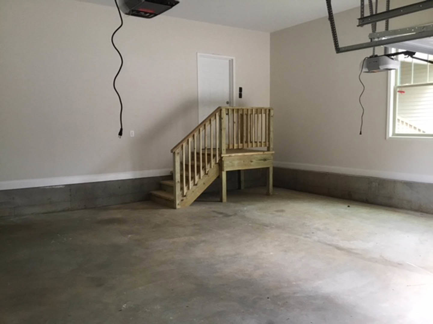Wooden staircase with metal handrail in a garage, laminate flooring, plaster walls, and a window visible in the background