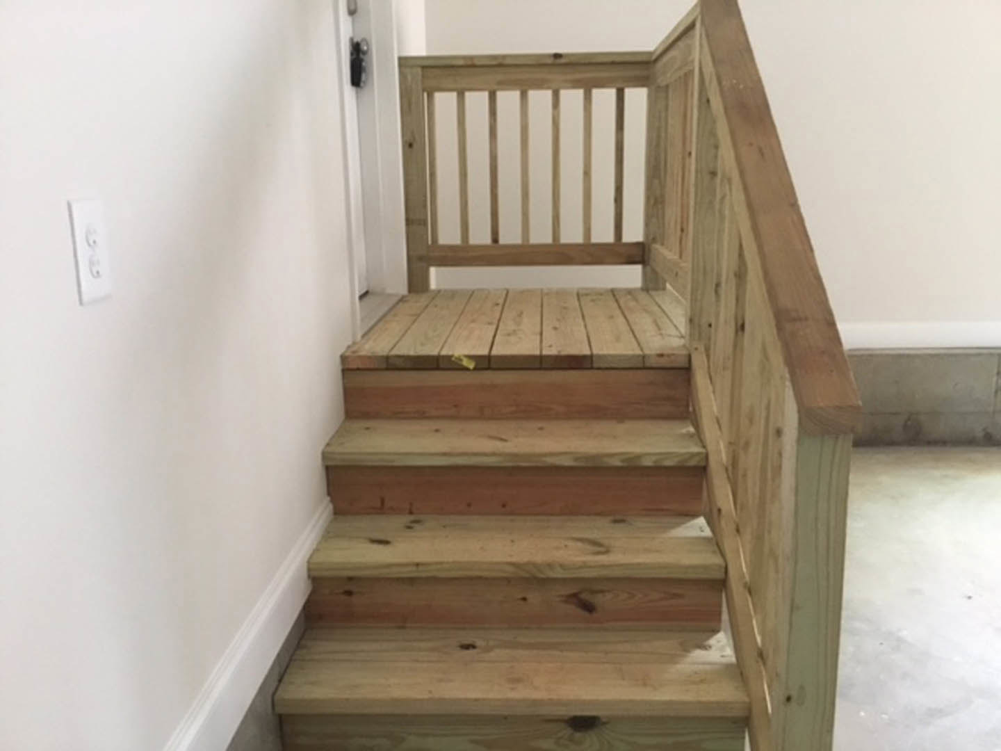 Hardwood staircase with vertical wooden balusters, white wall alongside, and wooden table with yellow decor in background