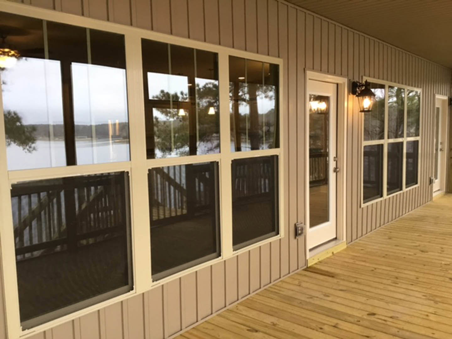 Wooden deck with large windows and glass door, covered porch area, light wood flooring, white walls, built-in bookshelf, screened wall section