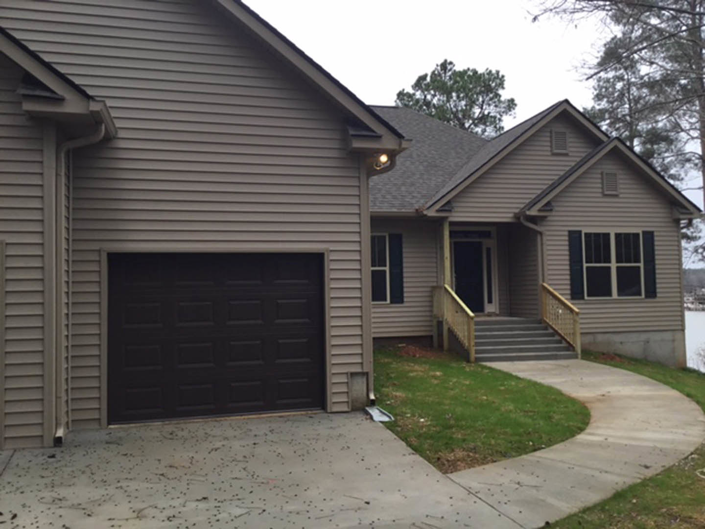 Modern home exterior with black garage door, white roof, white-framed windows, concrete driveway, green grass lawn, and front steps leading to entry