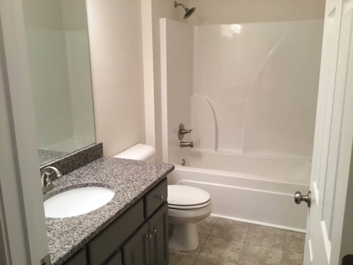 Bathroom with marble countertop, undermount sink, white toilet, glass-enclosed shower, tile flooring, and white walls
