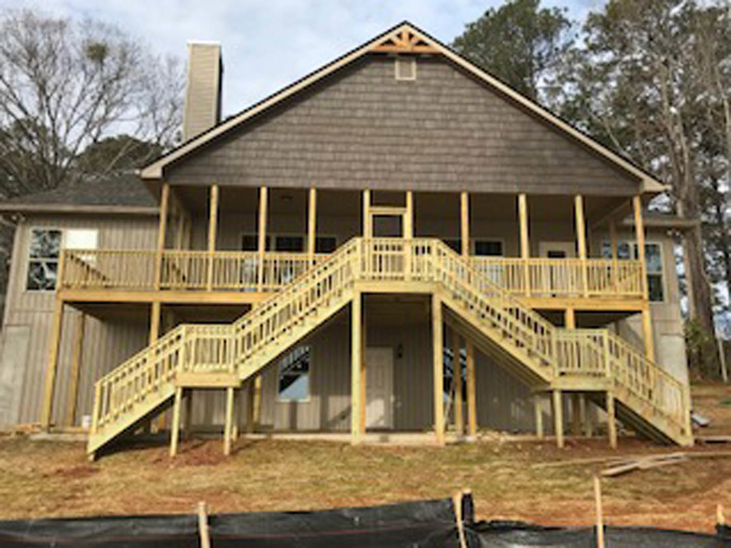 Two-story home with wood siding, small front porch, and short staircase leading to entry; trees and blue sky in background