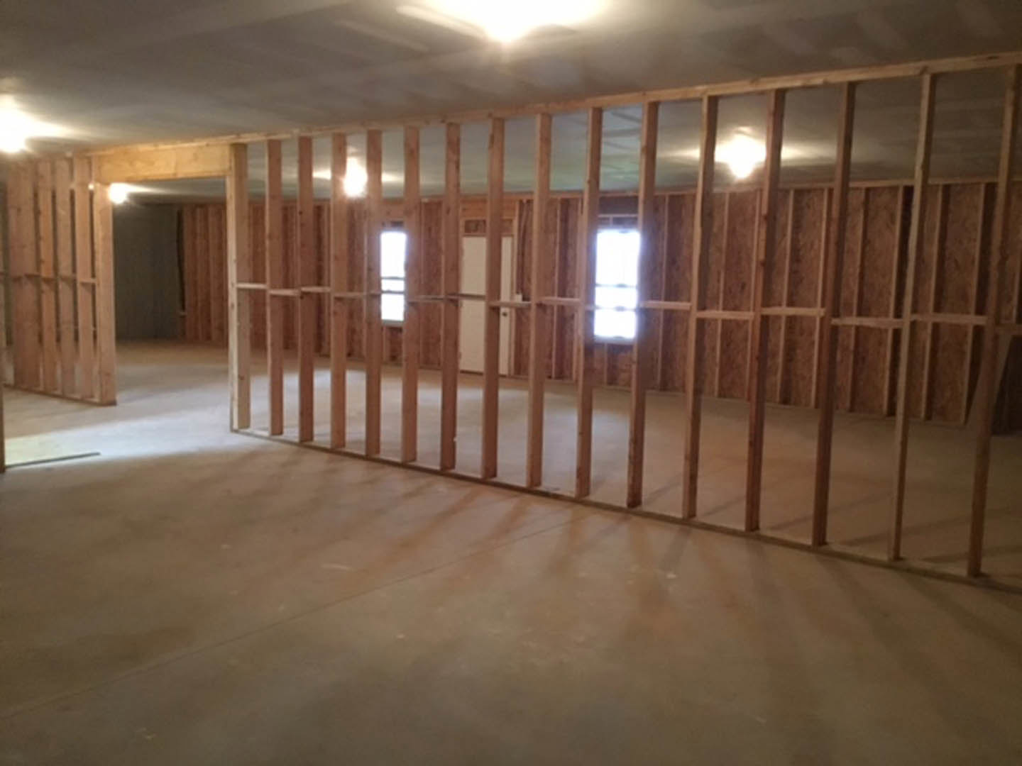 Open room with exposed wood ceiling beams, concrete floor, large window letting in natural light, and wood-paneled wall
