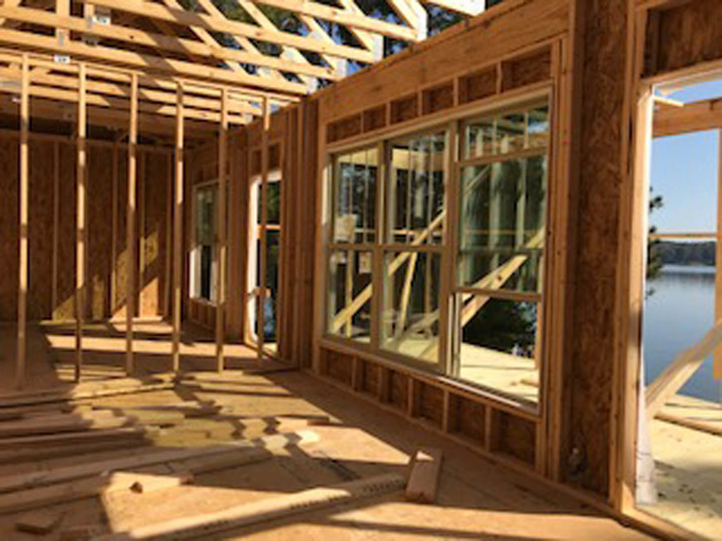 Wood-framed custom home under construction with installed windows, exposed beams, and unfinished lumber; person visible in background near staircase.