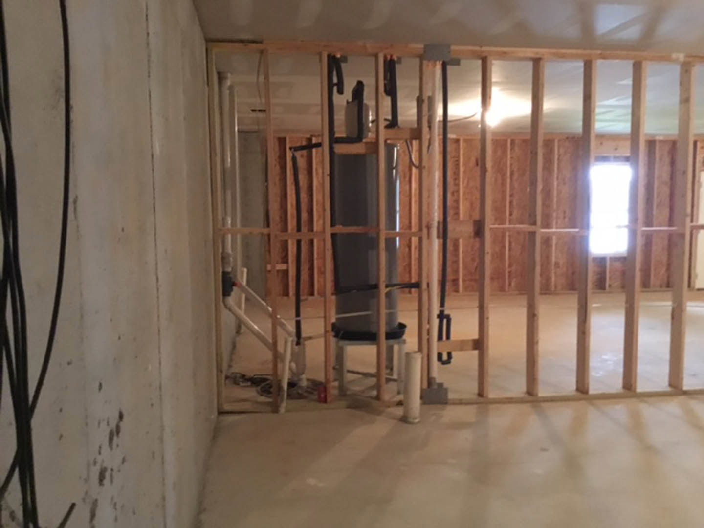 Concrete floor with a large grey cylinder and white pipe against a plastered wall, wood door partially visible, black wire in foreground