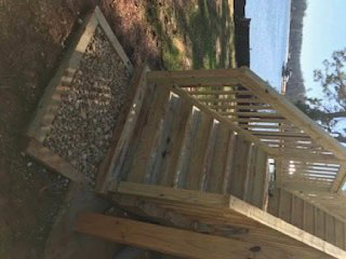 Wooden outdoor staircase with railing leading down to grassy area, river and trees visible in the background