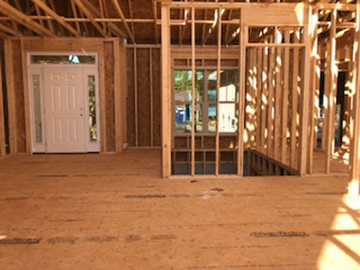 Wood-framed room with exposed beams, white door featuring glass panels and metal doorknob, wooden plank flooring, and window allowing natural light