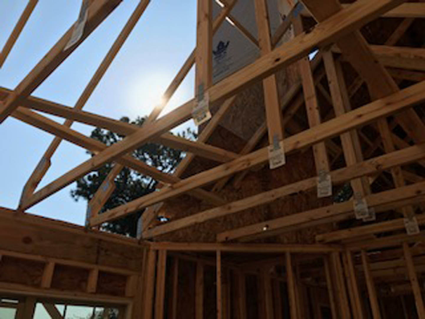Exposed wood framing and beams forming the structure of a house under construction, with blue sky visible above