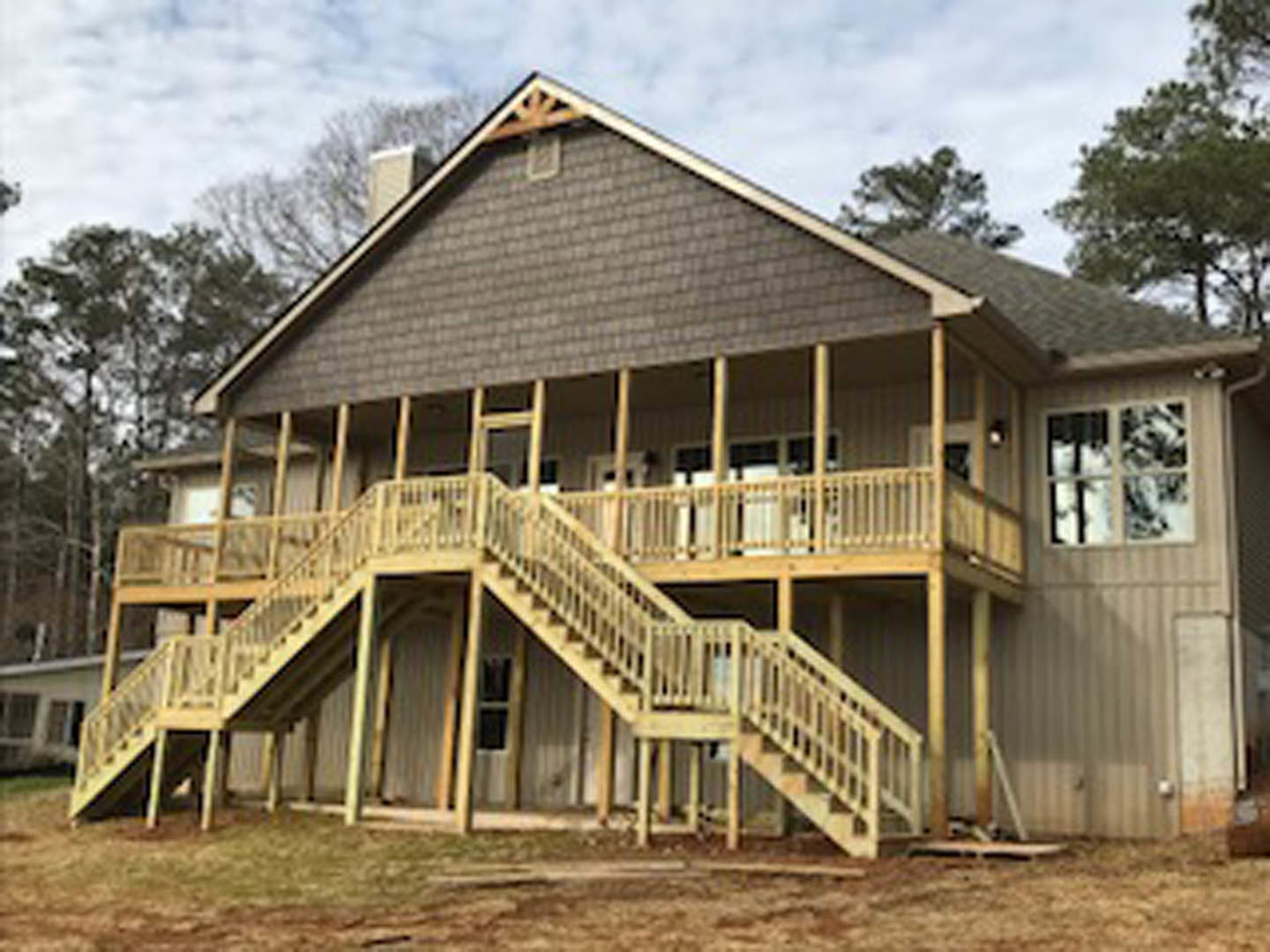 Two-story home with wood siding, covered porch, and front stairs, surrounded by trees and open dirt field, Sánchez Adobe Park visible in the background.