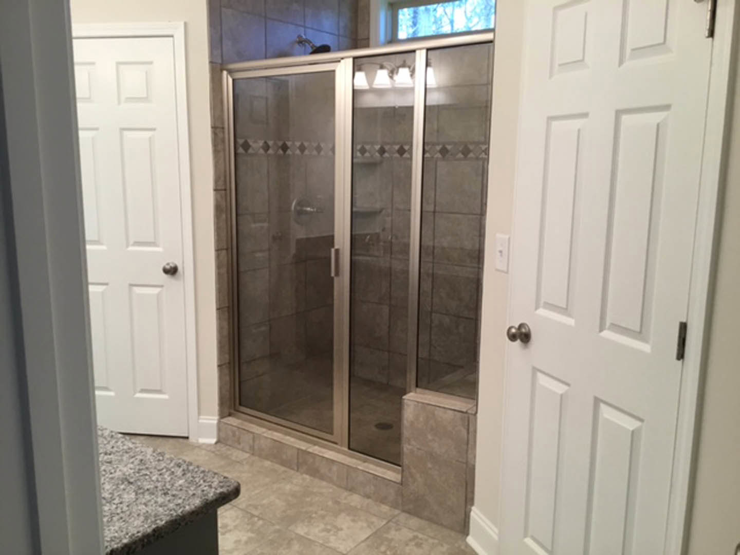 Walk-in shower with clear glass doors, large gray tile walls, and chrome fixtures adjacent to a white vanity countertop