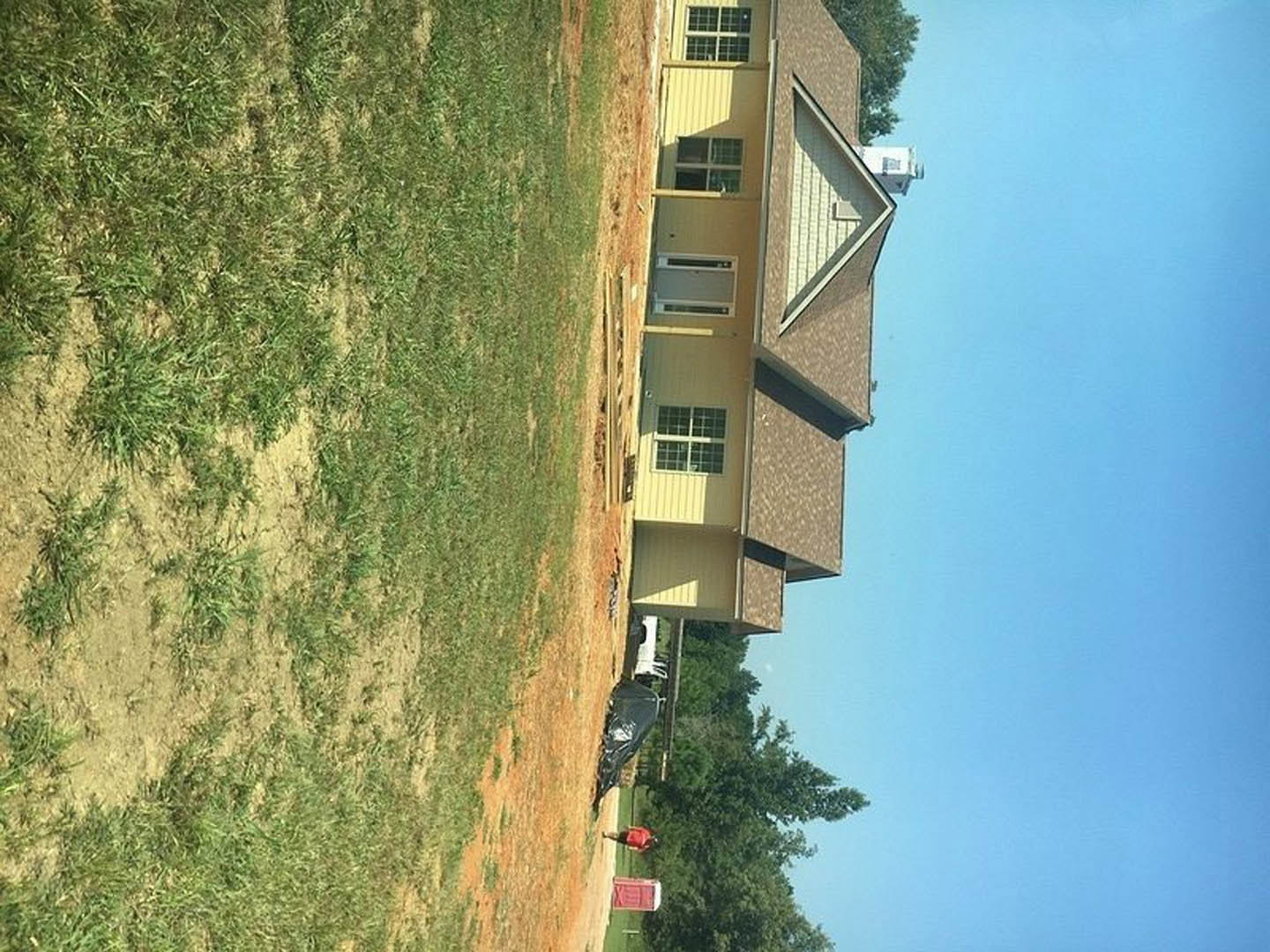 Two-story custom home with white siding and large windows, surrounded by a spacious green lawn and mature trees under a clear sky