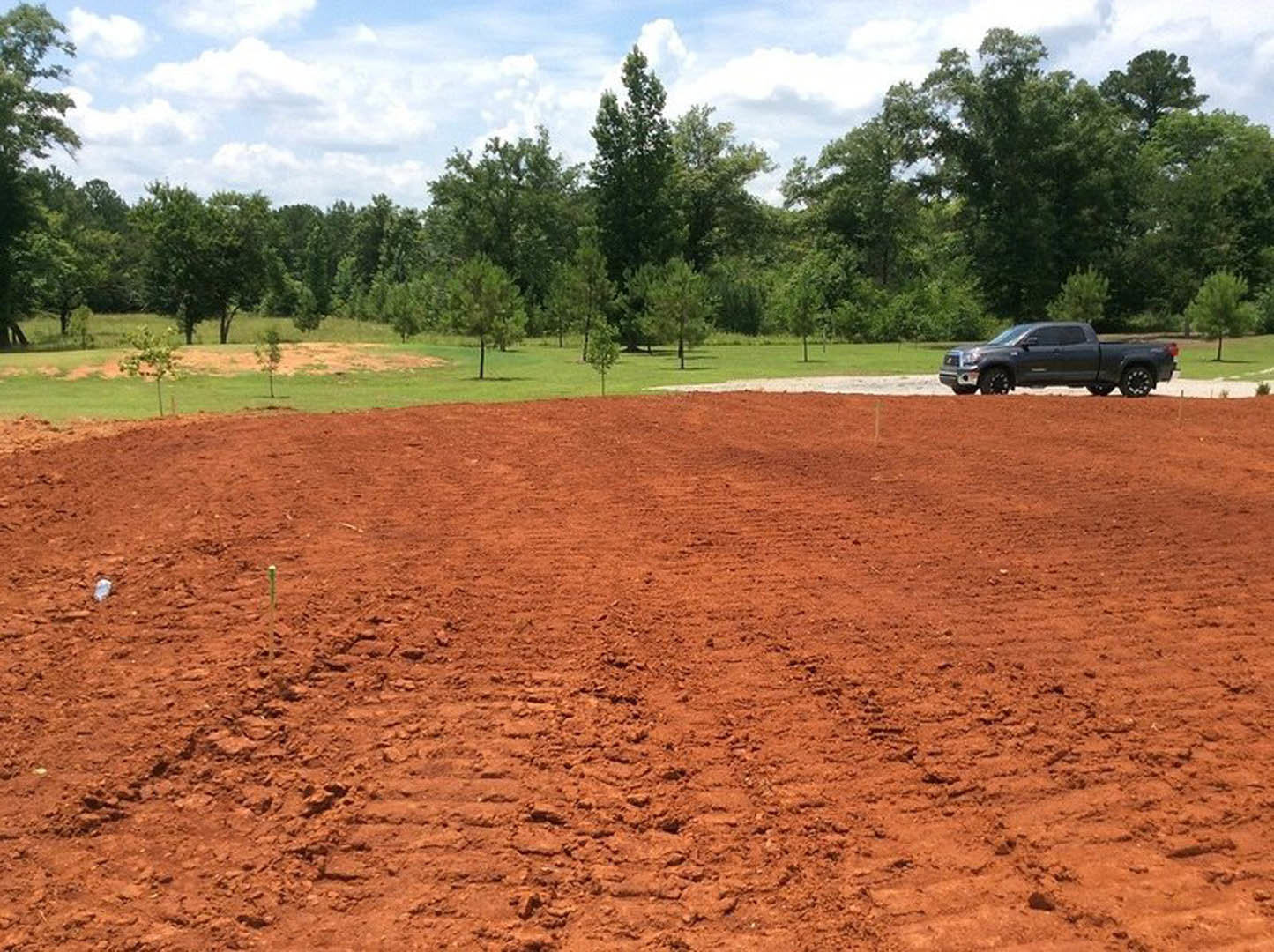 Black pickup truck parked on dirt field with scattered trees and cloudy sky in background