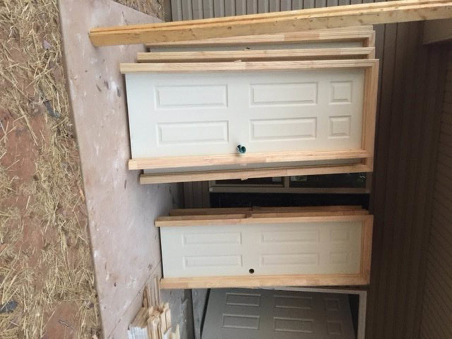 Cluster of white doors with cutouts and pipes, surrounded by unfinished wooden beams and grey plywood surfaces in a construction area