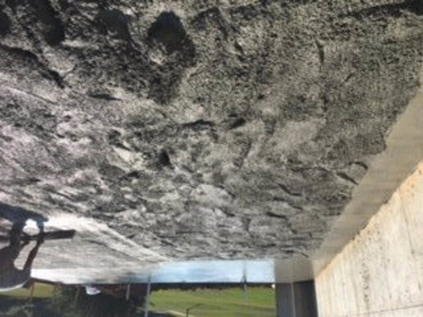 Concrete exterior wall adjoining textured stone wall, outdoor mountain setting with rocky ground.