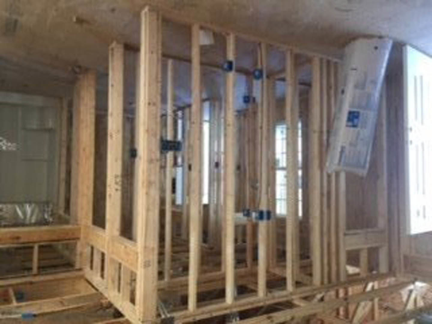 Exposed wood framing and beams inside a house under construction, with plywood sheathing and insulation visible
