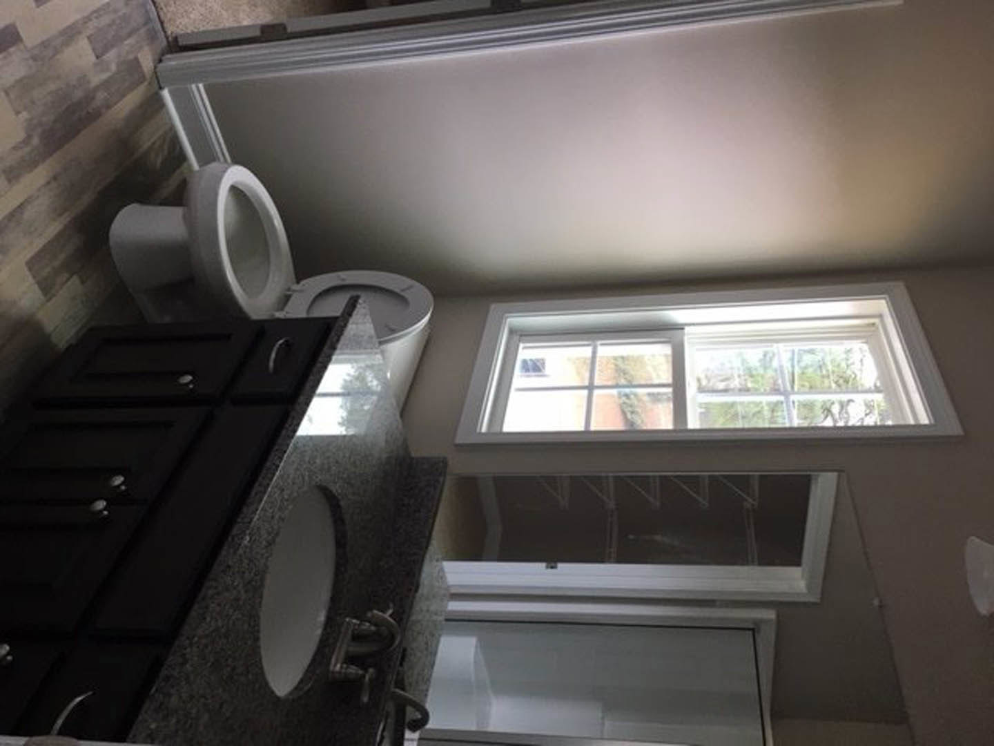 Modern bathroom featuring a white toilet beside a black vanity cabinet with integrated sink, light-colored walls, and a window providing natural daylight.