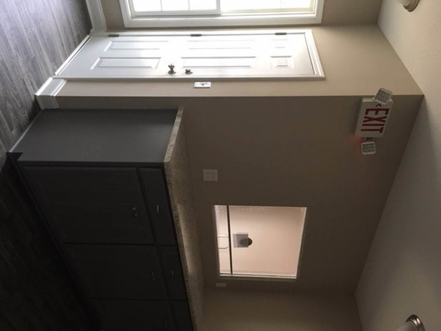 Bathroom with white walls, single window with black trim letting in natural light, and a closed door adjacent to the window.
