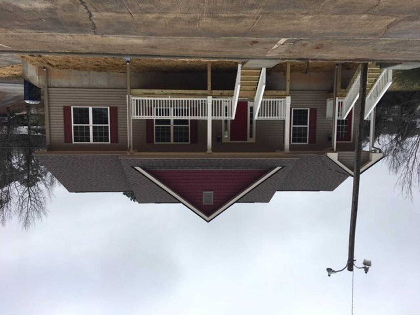 Two-story home with snow-covered roof, white porch railing, white-framed windows, and a street light in front; bare trees and winter landscape visible.