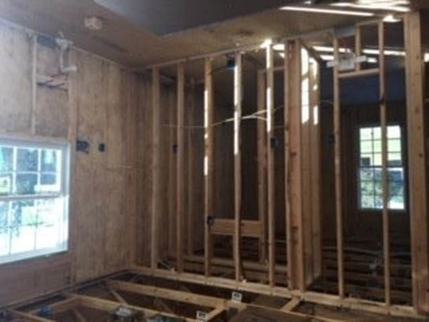 Unfinished room with exposed wood framing, plywood subfloor, and visible beams; construction materials and insulation present