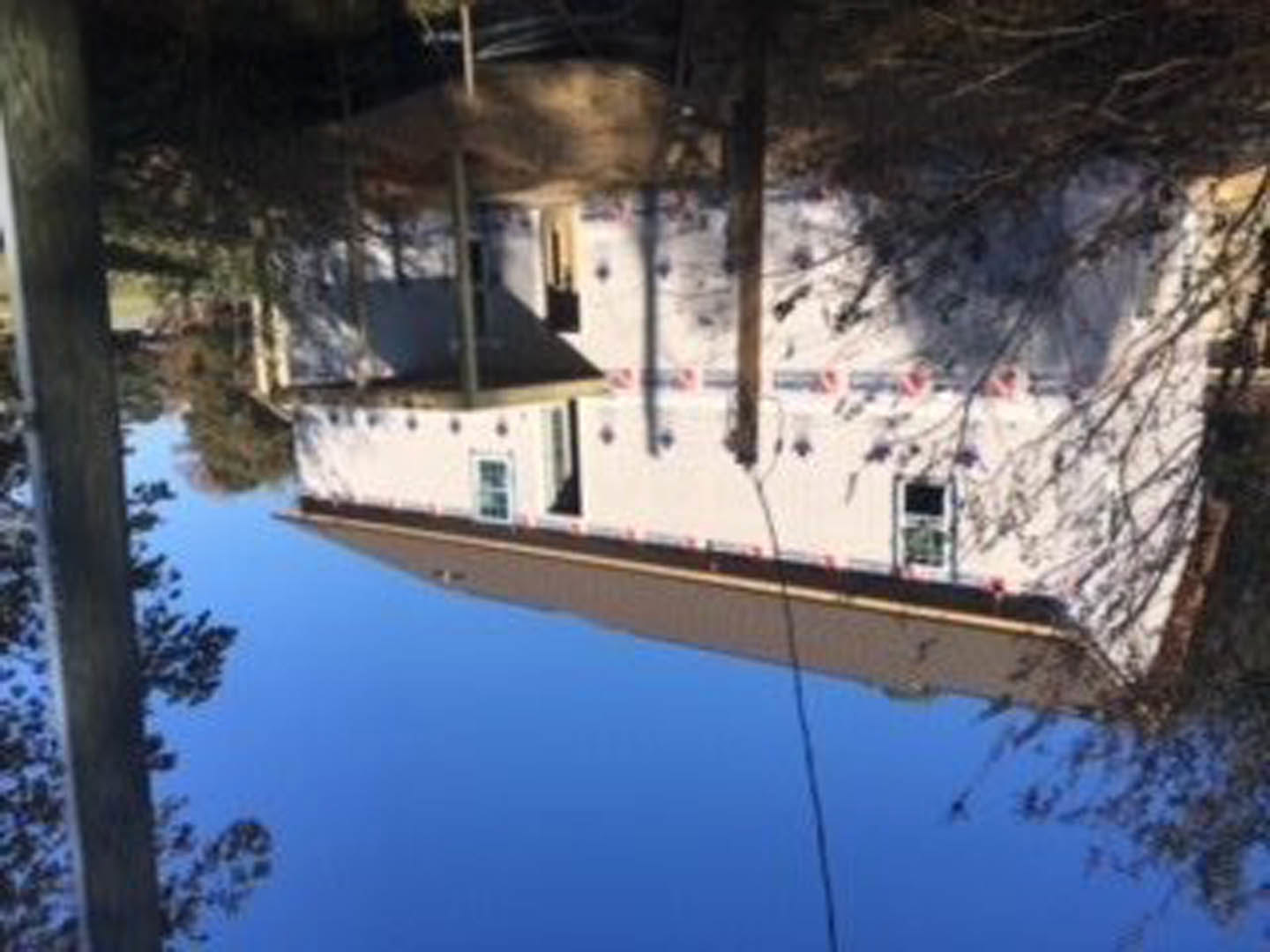 White modern home exterior with crisp lines, blue sky backdrop, red and white striped accent, tree nearby, building reflected in calm water.