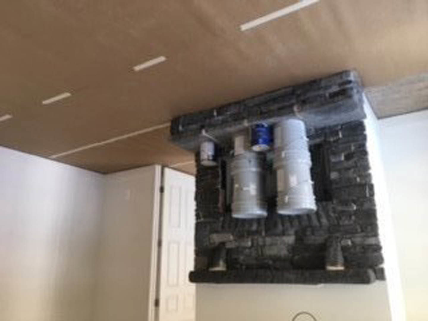 Brick fireplace with plaster walls, two grey barrels near hearth, white ceiling, fire extinguisher mounted on wall