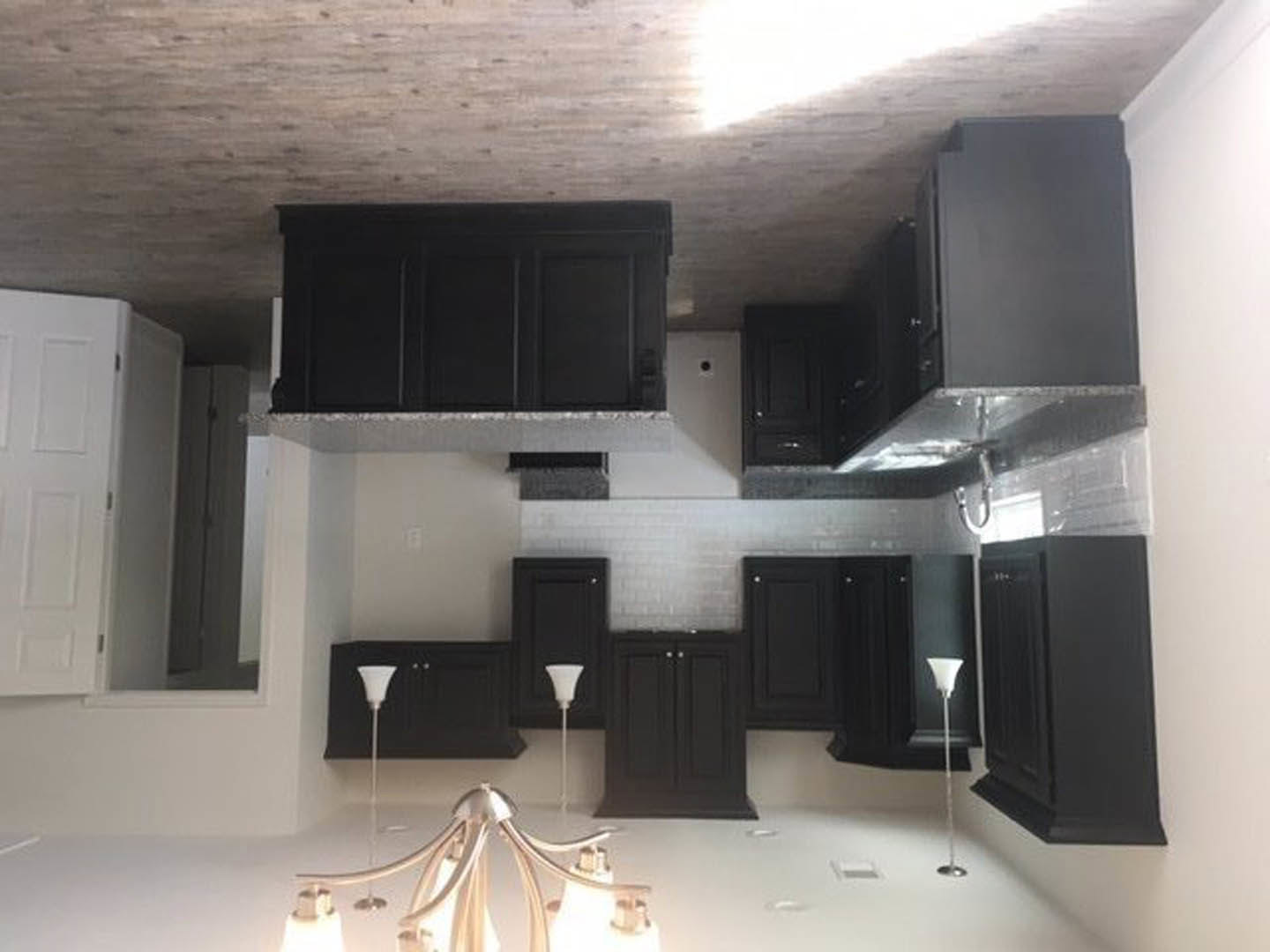 Kitchen with matte black cabinets, white walls, and ceiling; modern light fixture overhead; close-up of black door and cabinet; white pole with black stripe; person's hand holding