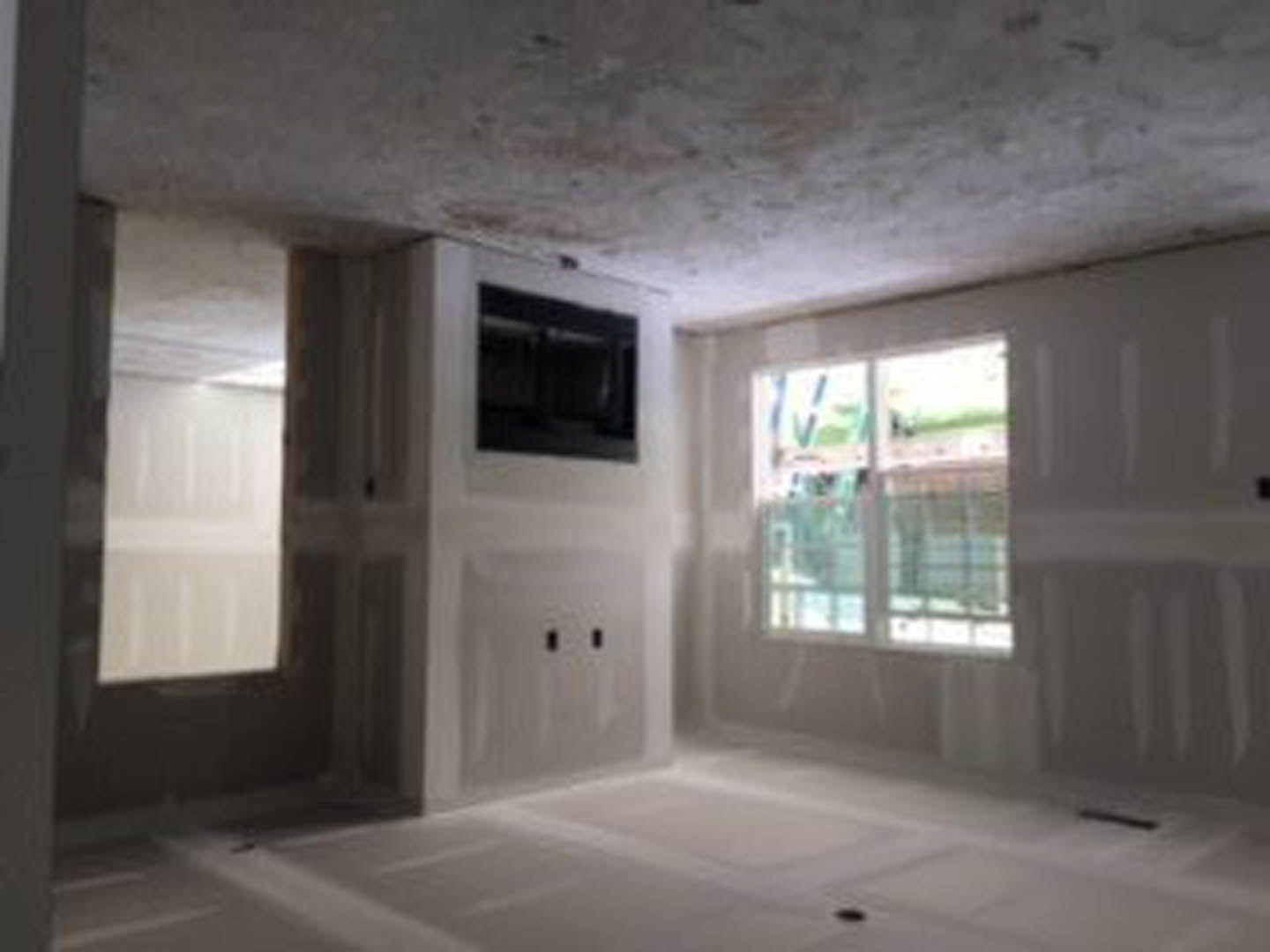 Living room with large window, mounted flat-screen TV, white plaster walls, crown molding, and hardwood flooring