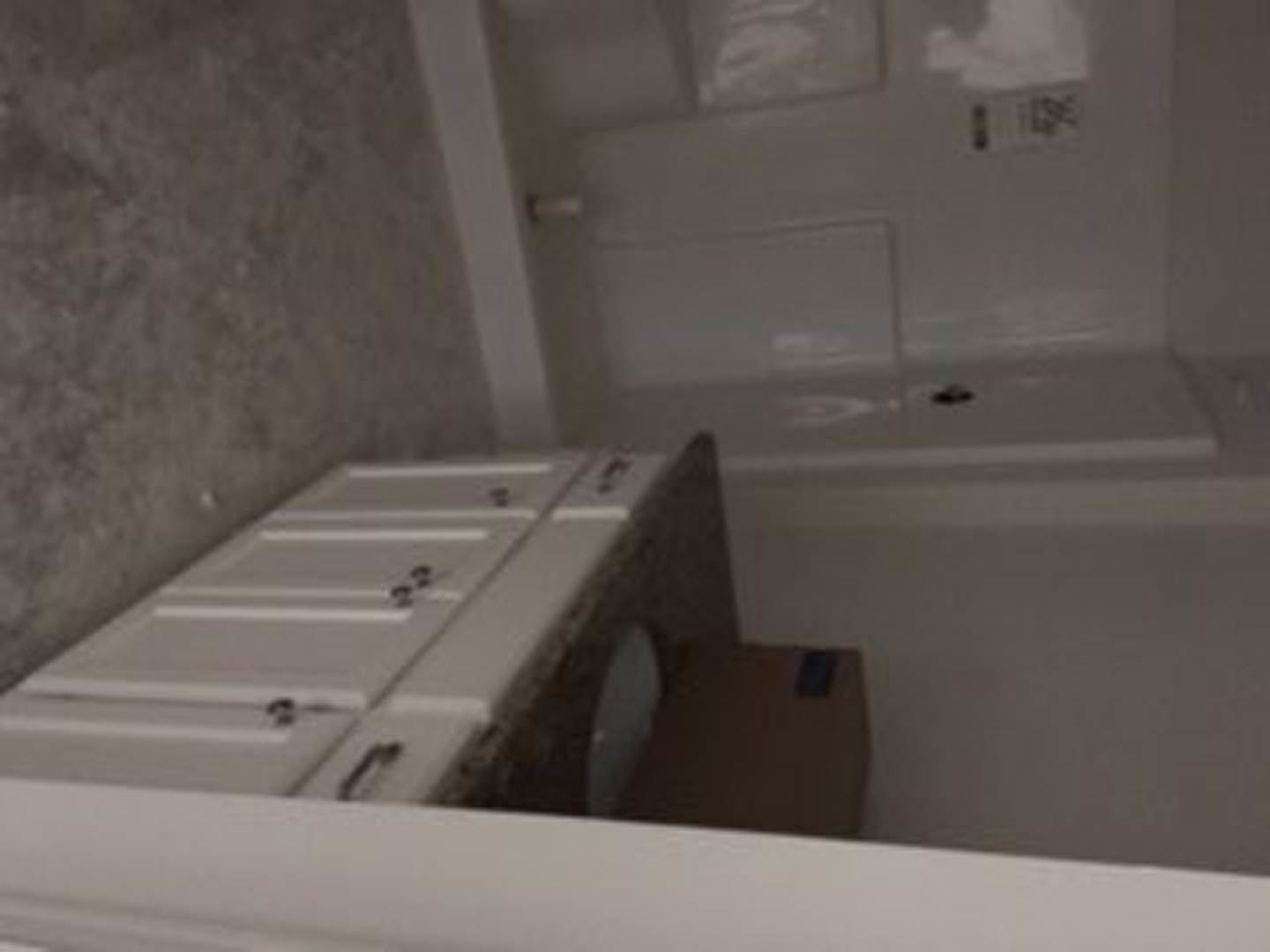 Modern bathroom featuring a white vanity with black handles, undermount sink, chrome faucet, and a toilet; light gray walls and a partial view of a bathtub with glass shower