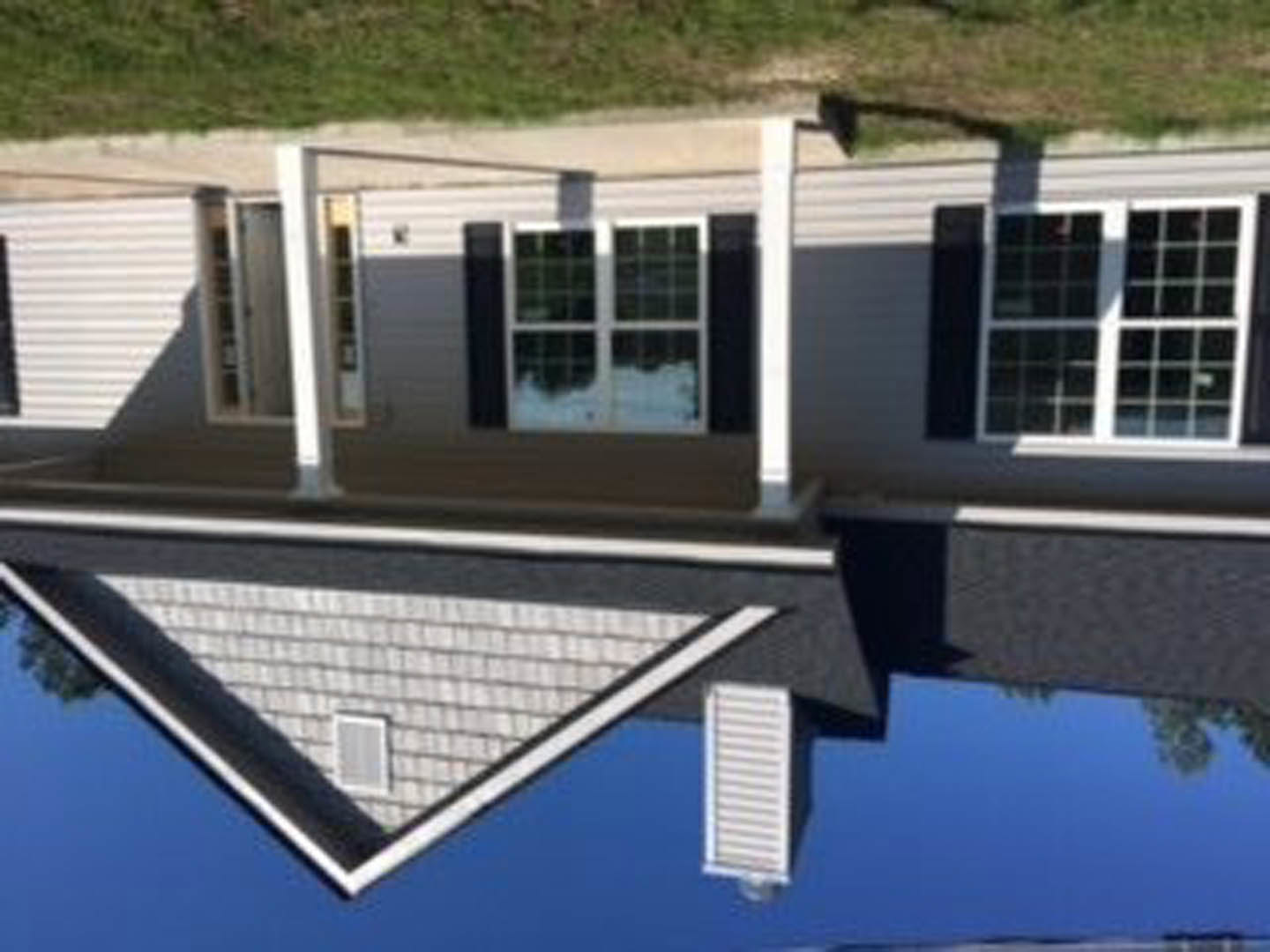 Two-story house with gray composite siding, white trim, large windows, gabled roof, manicured green lawn, and clear blue sky in background