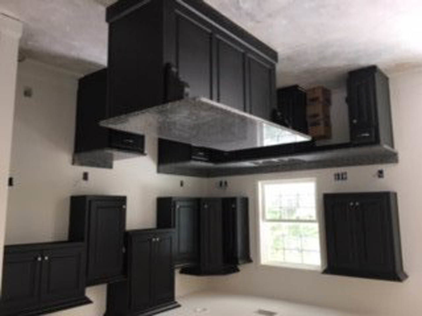 Black kitchen cabinets with stainless steel appliances, light stone countertops, and a modern range hood against a neutral wall.