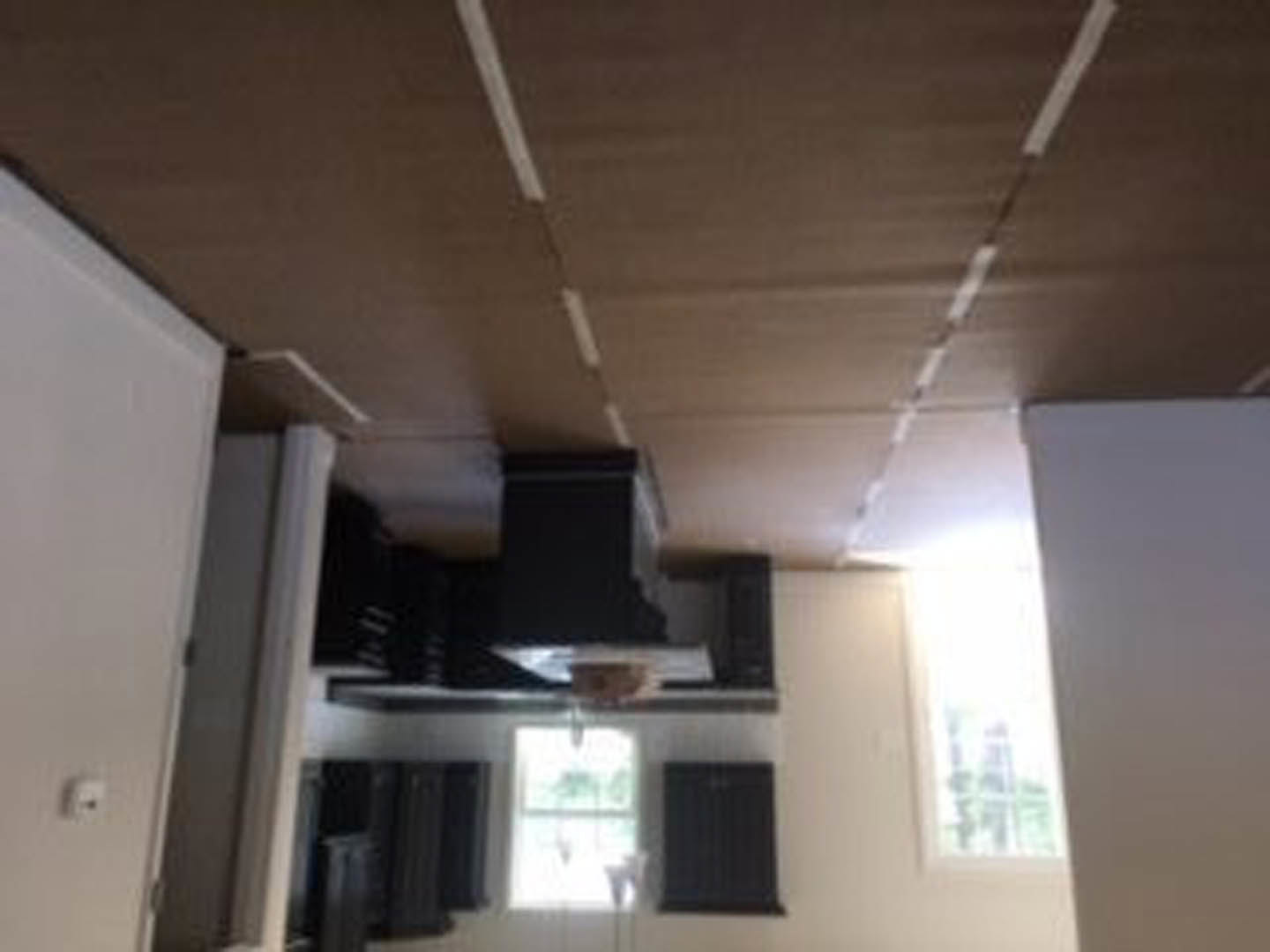 White plaster ceiling above a white wall with recessed lighting, black built-in cabinets along one side, blurred figure partially visible in foreground