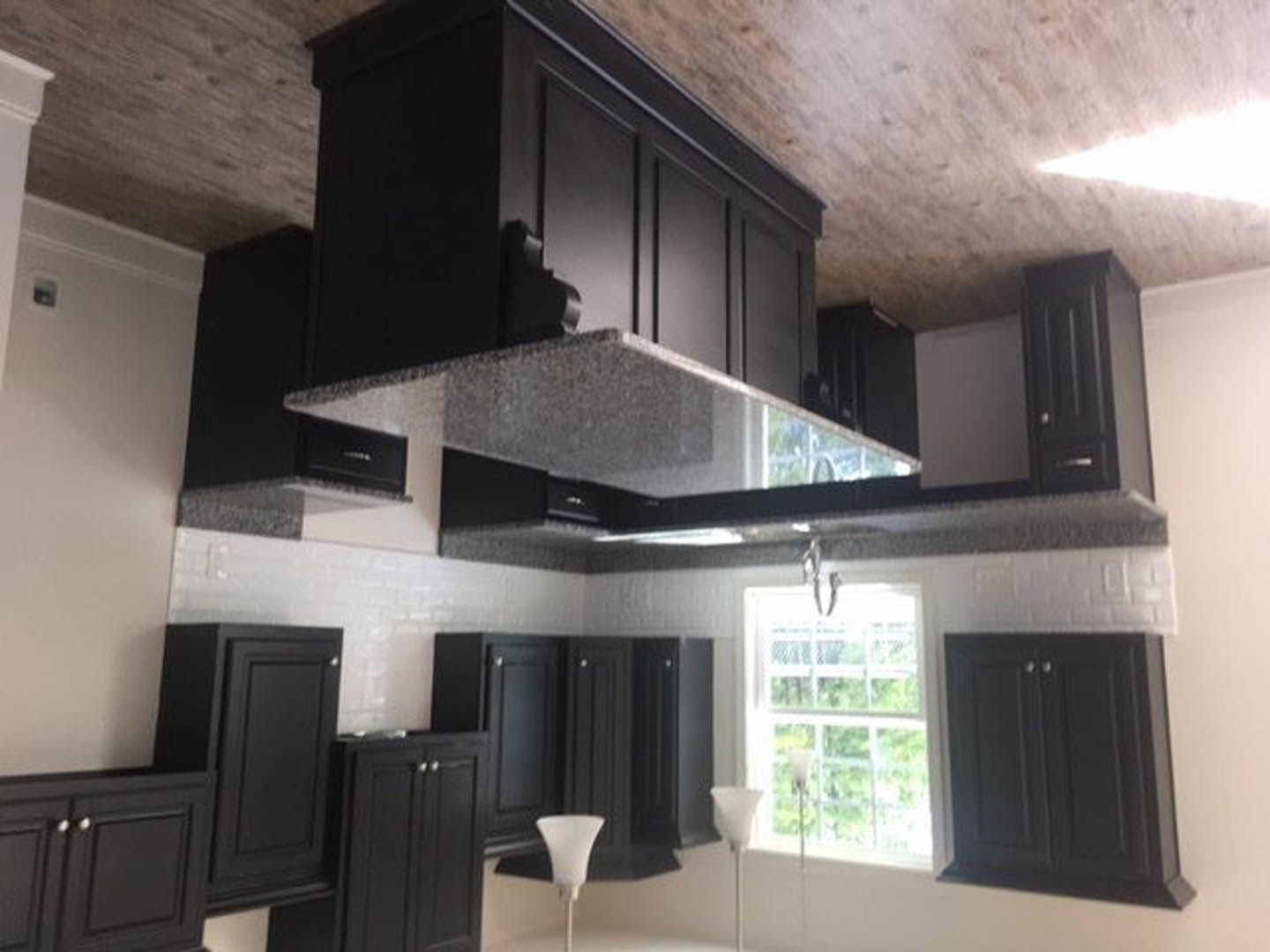 Black kitchen cabinets with a white countertop, white lamp, and white vase; window with white frame in the background.