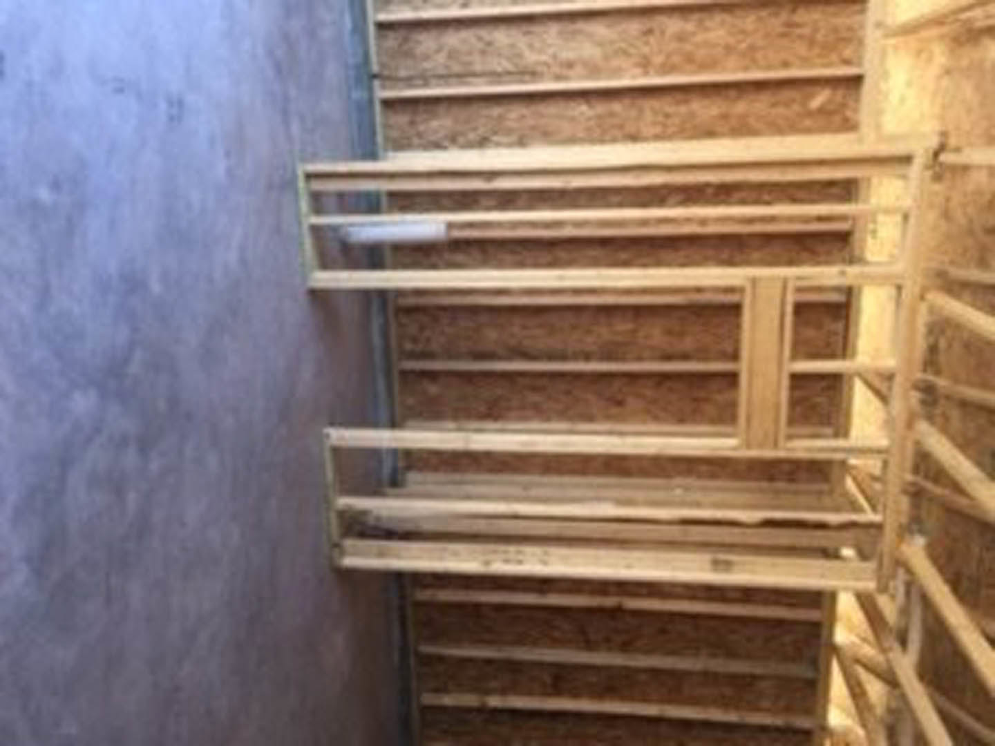 Wooden staircase frame with exposed lumber and handrail, ladder leaning against unfinished wall in a partially constructed room