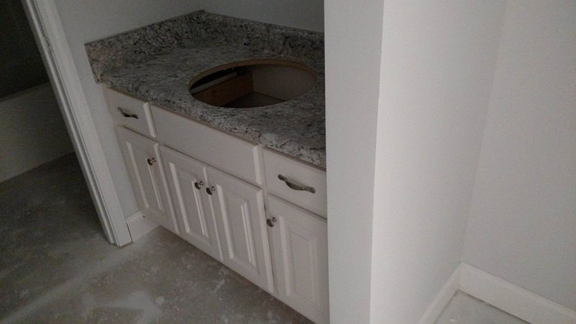 White bathroom sink set into a marble countertop with grey tile backsplash, white cabinetry below, and a chrome faucet.