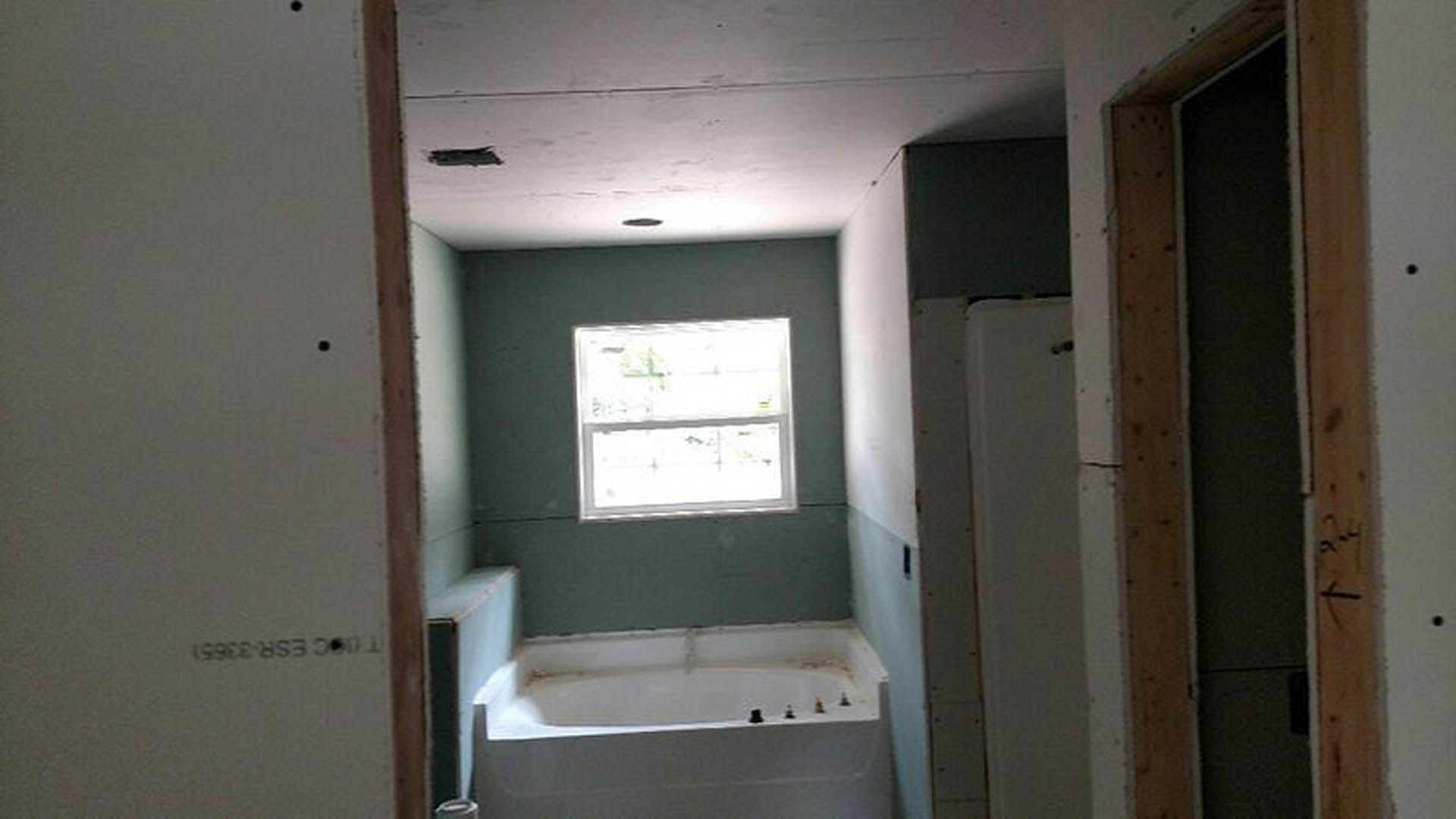 Freestanding bathtub beneath a large window, white tile walls, chrome plumbing fixtures, glass shower enclosure, light-colored flooring
