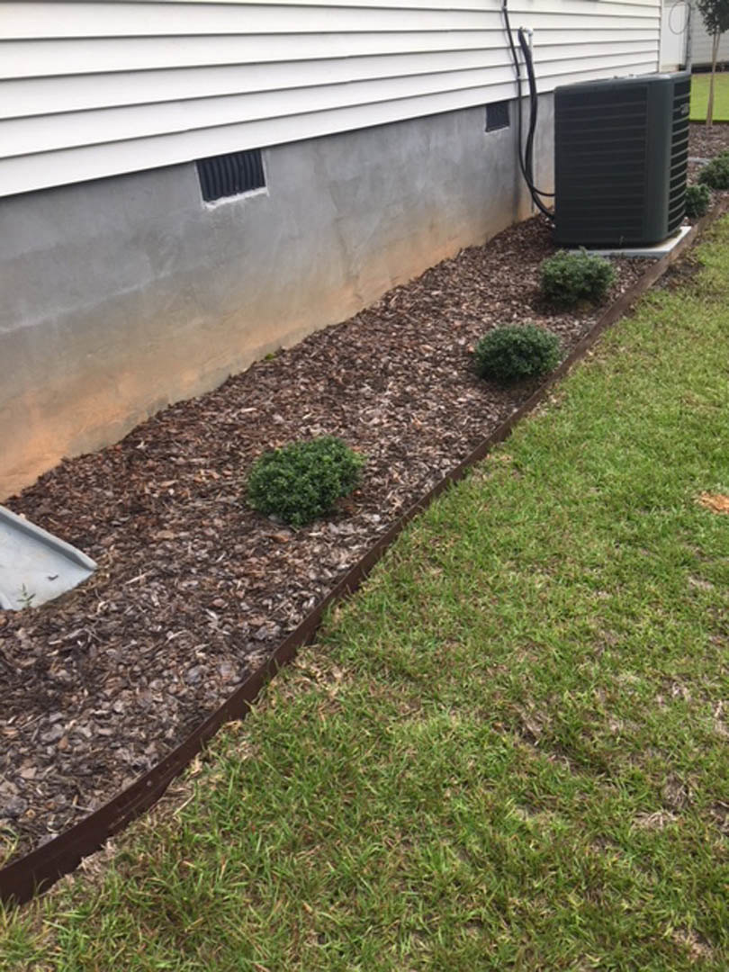 Front yard with green grass, mulched planter bed, concrete retaining wall, and modern house exterior in background