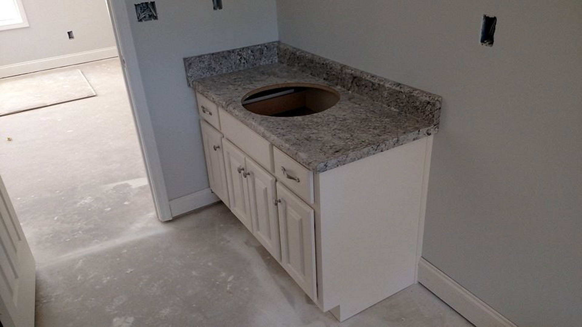 White undermount sink set in granite countertop with tile backsplash, white cabinetry, and sunlight streaming through nearby window